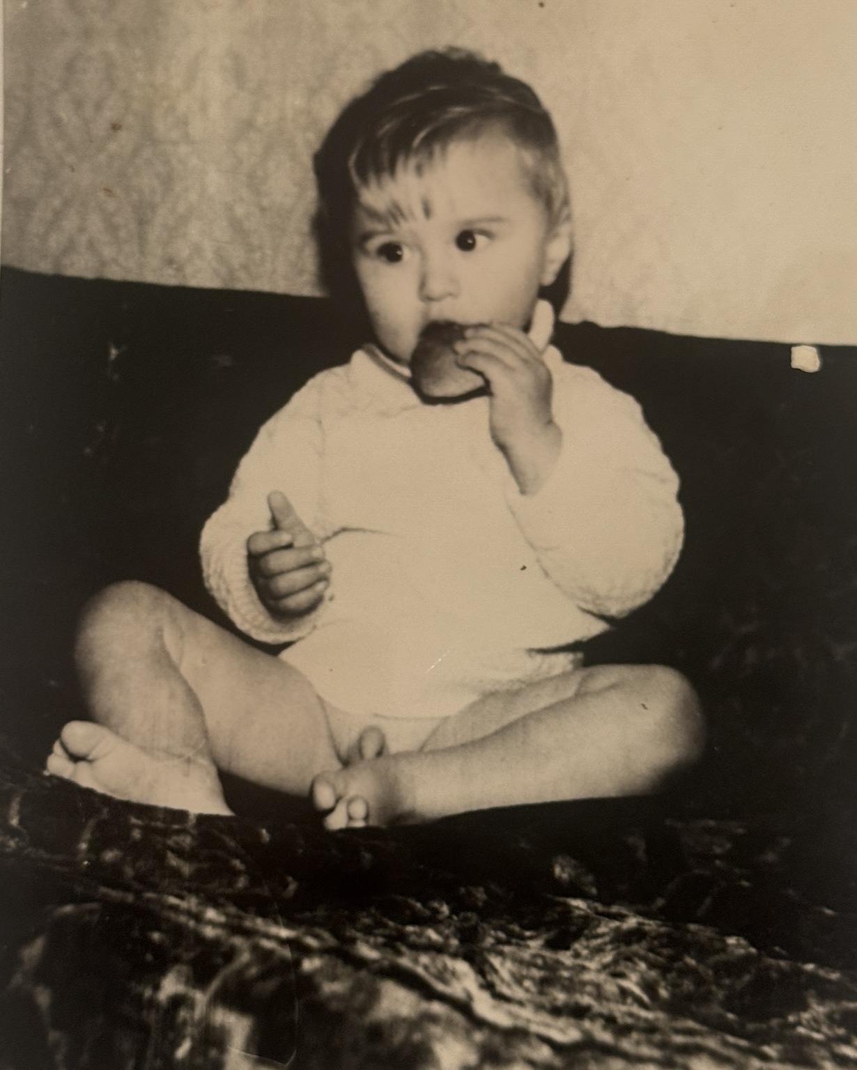 Фотография: ребёнок в светлой кофте сидит, поднеся еду ко рту.